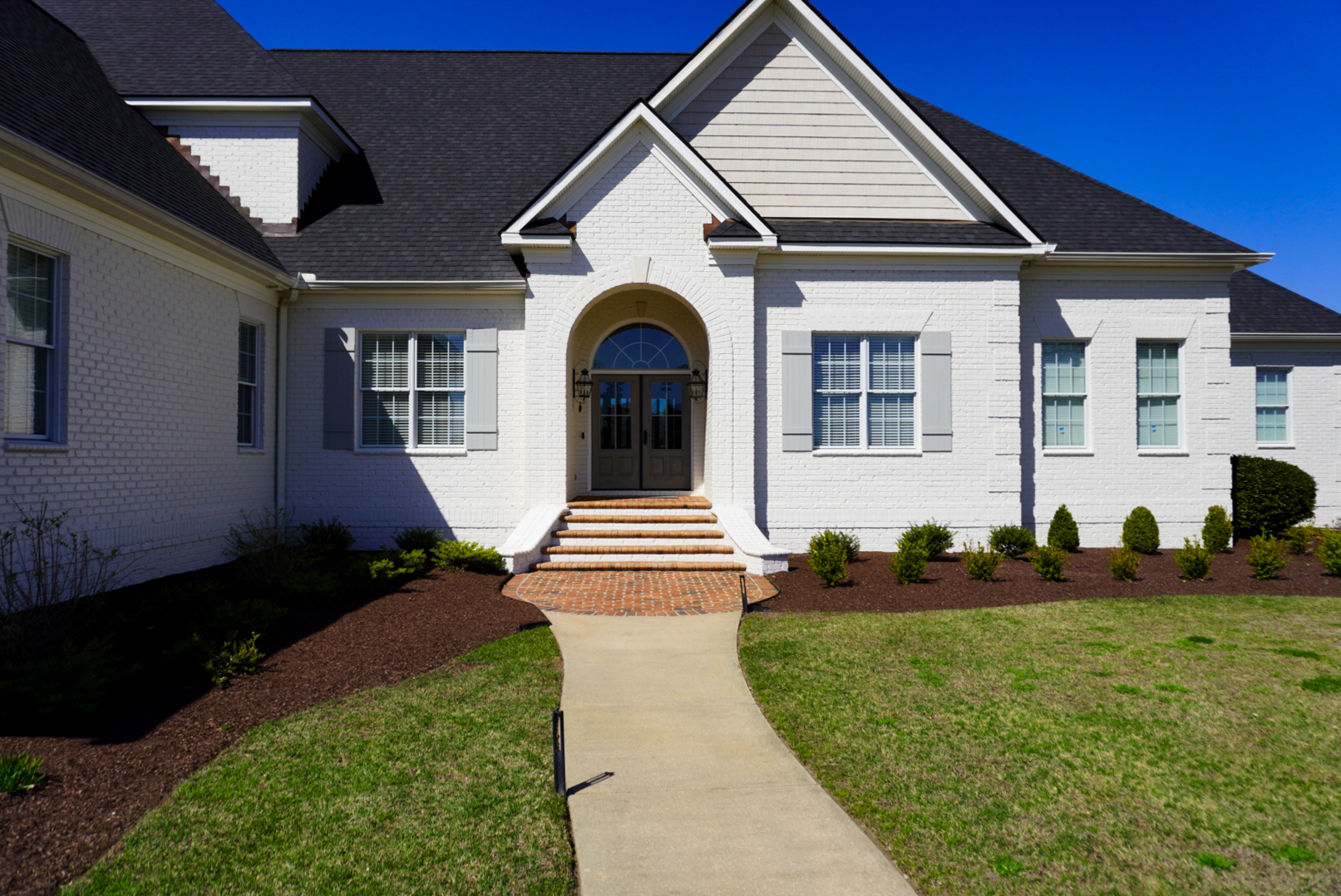 White-brick home with arched entry and formal landscaping.