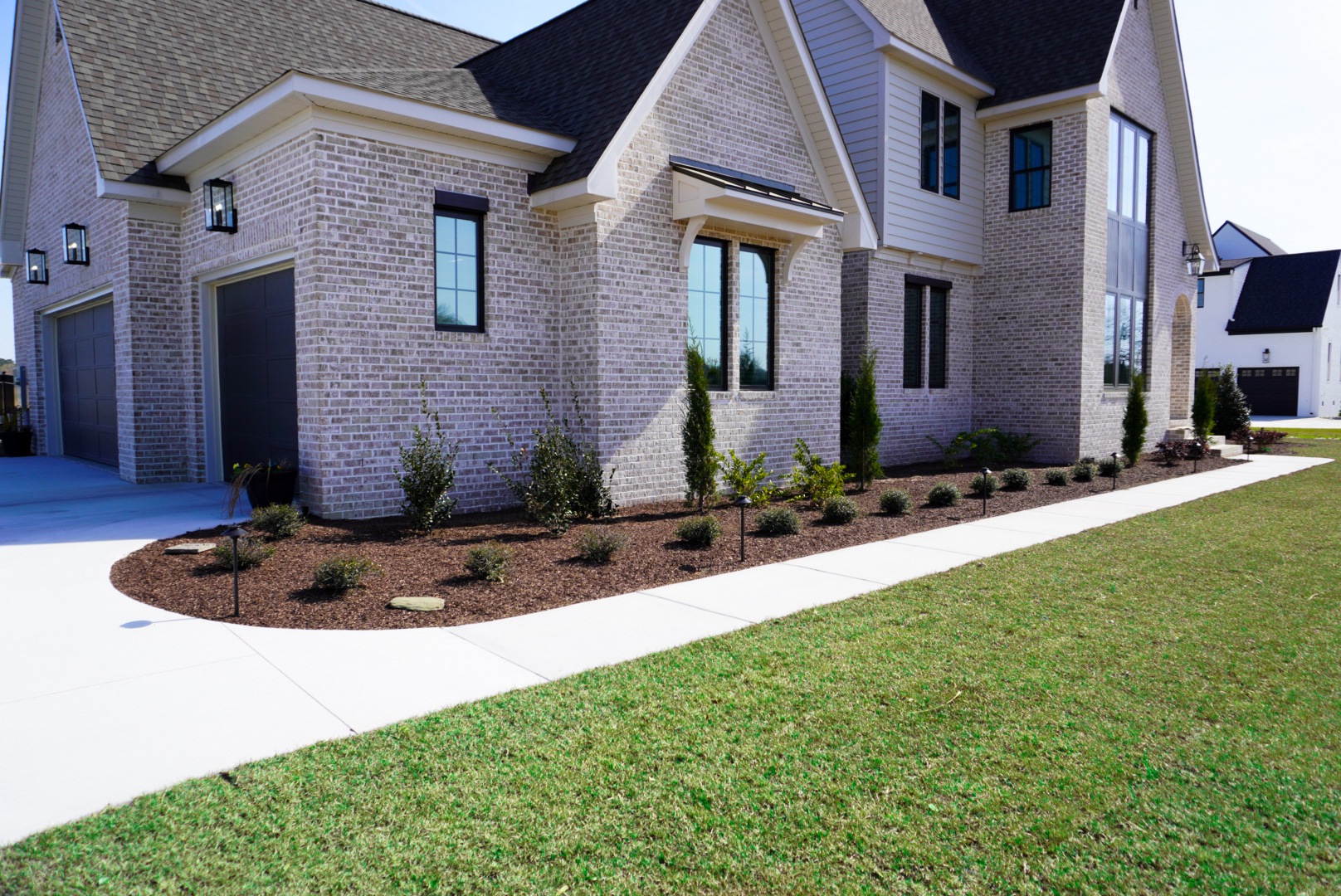 Tan-brick home — front driveway and foundation bed.