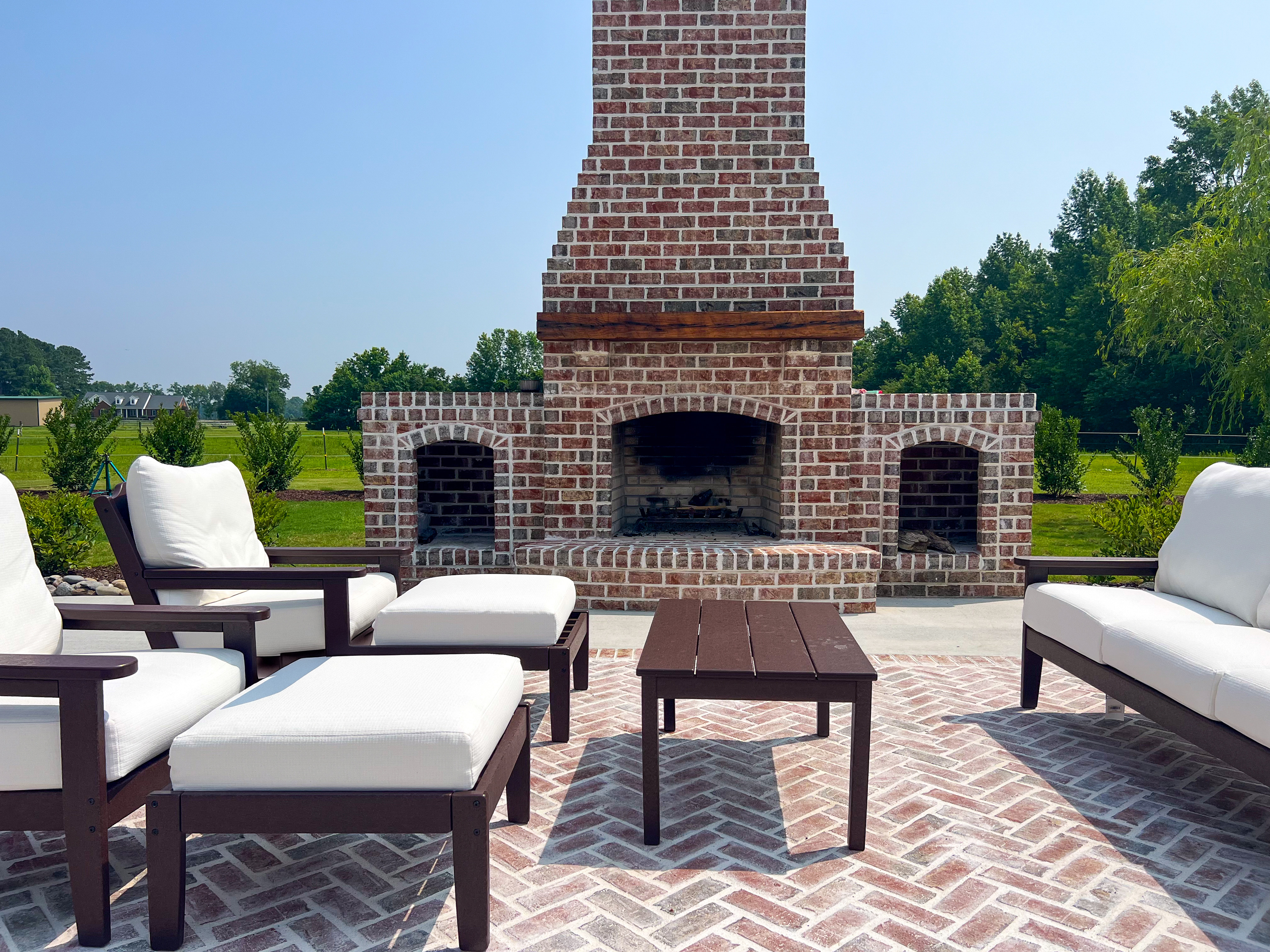 Hand-laid brick fireplace with white-cushion lounge on a herringbone brick patio.