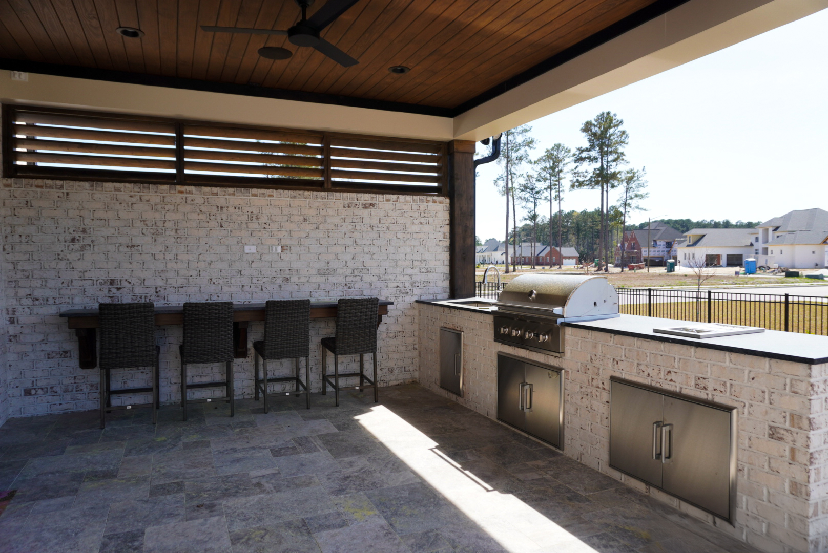 Covered outdoor kitchen with built-in grill, bar seating, and travertine floor.