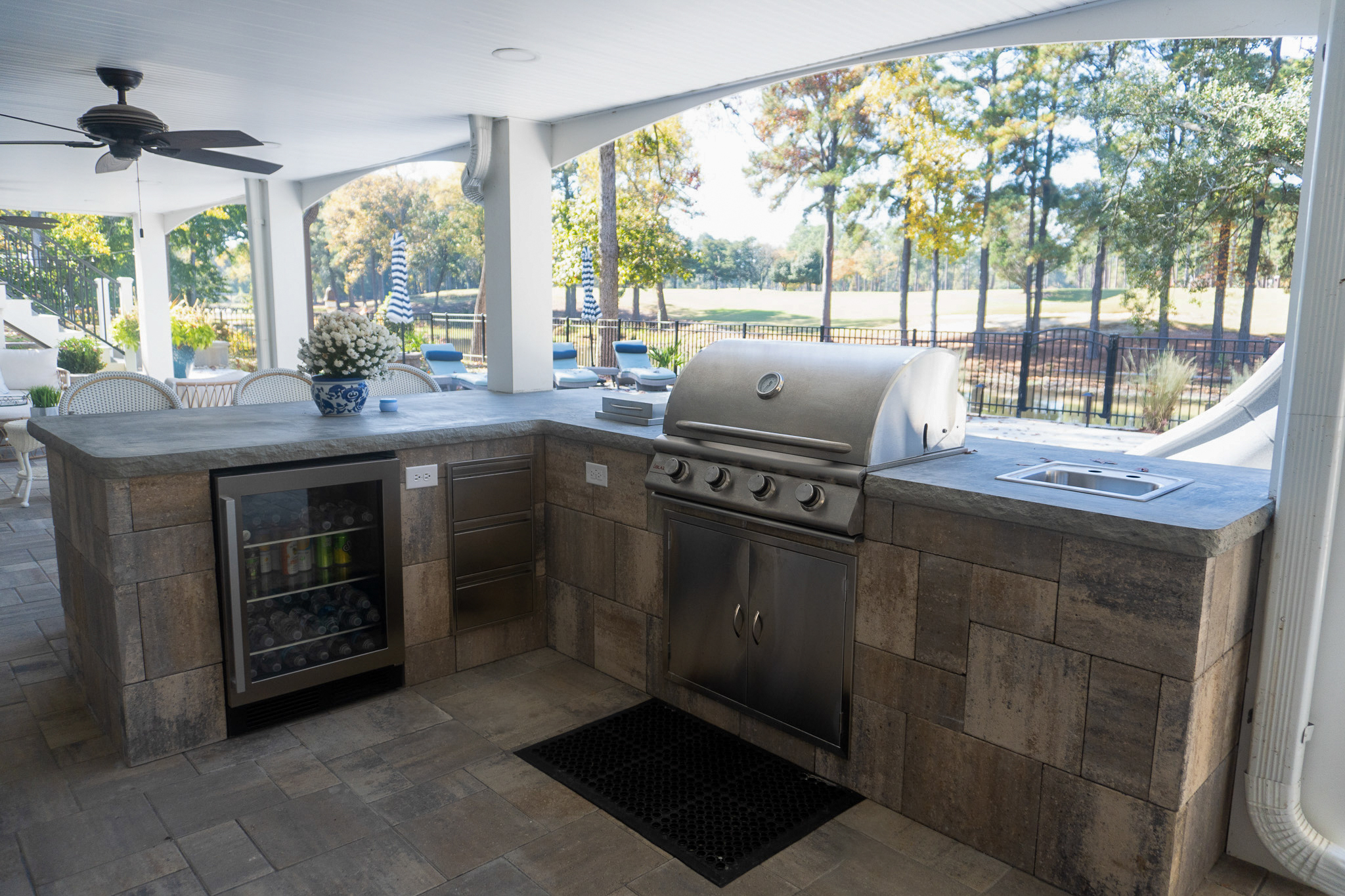 Built-in stainless grill, wine fridge, and stone-clad cabinetry under a covered patio.