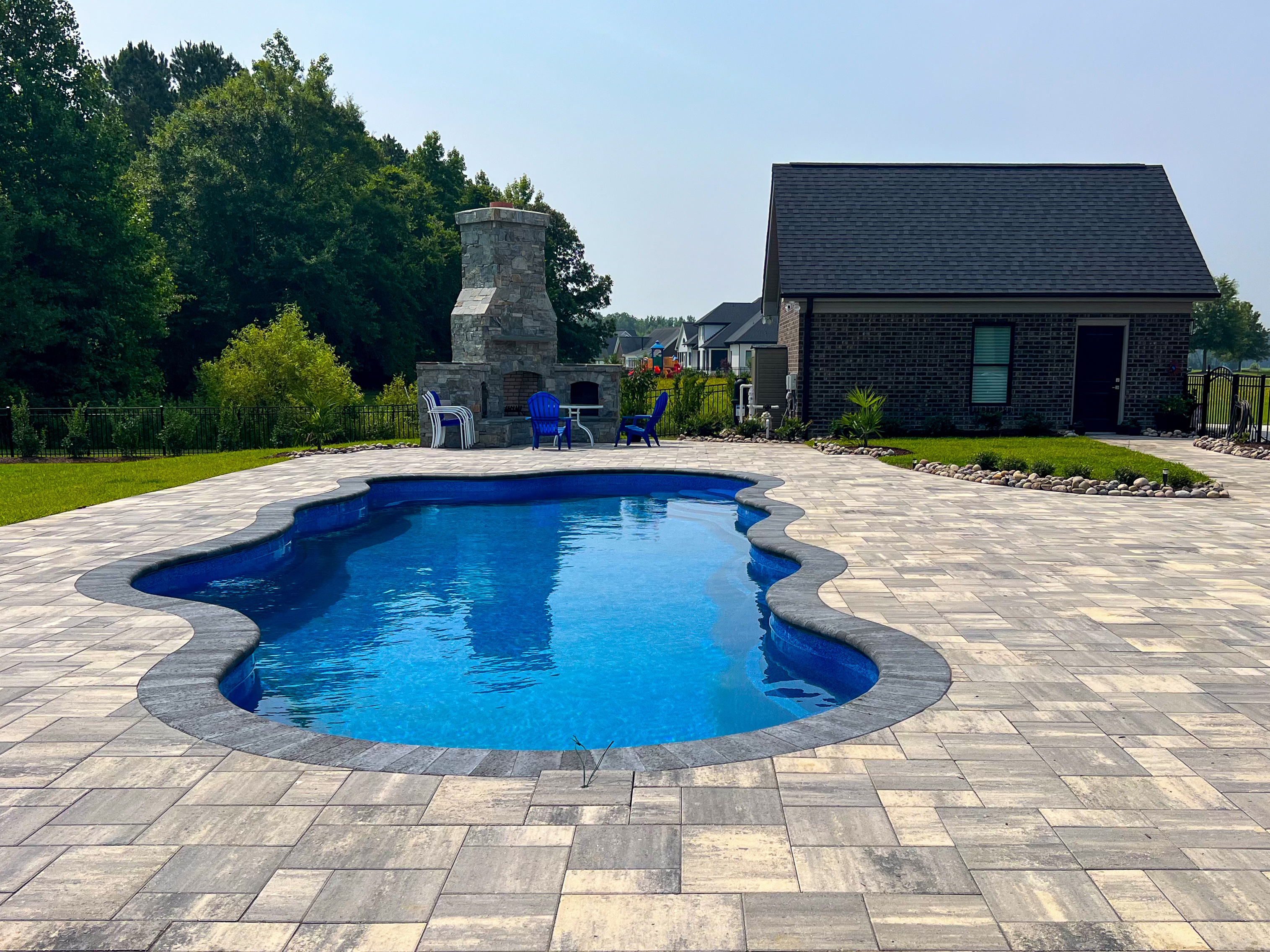 Freeform pool with stone fireplace and paver deck.