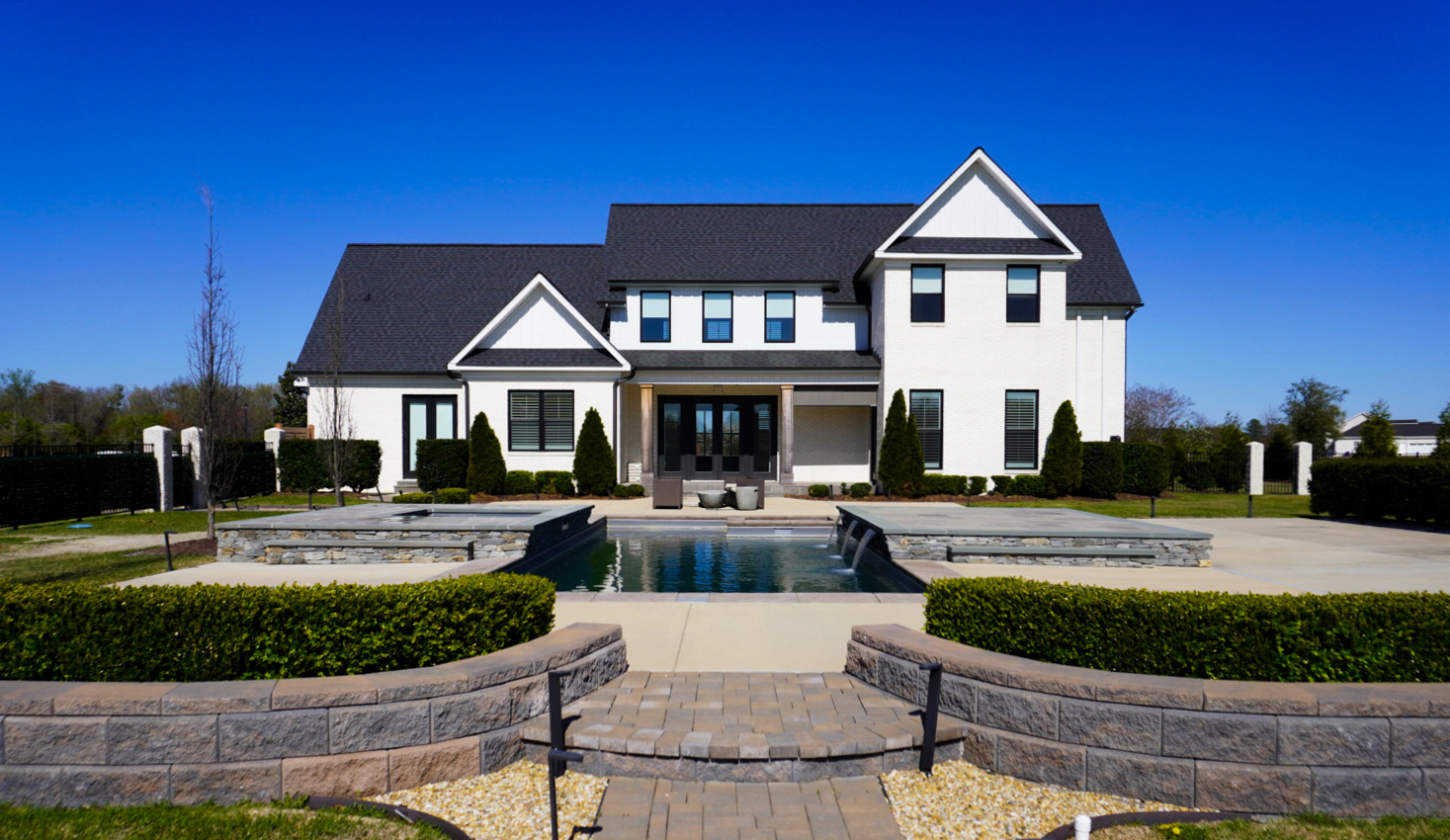 Modern farmhouse rear with pool and retaining walls.